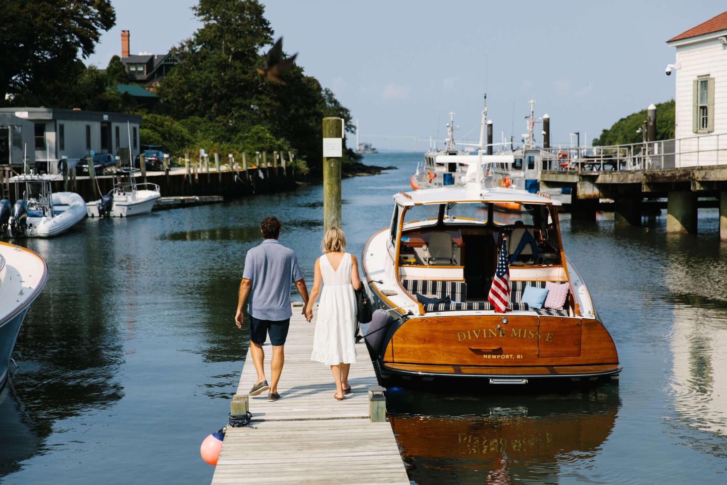Couple walking on a dock towards a wooden boat on a sunny day.