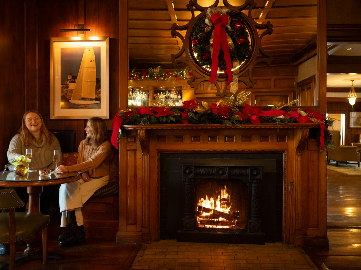 Cozy room with a lit fireplace, holiday decor, and two people chatting at a table.