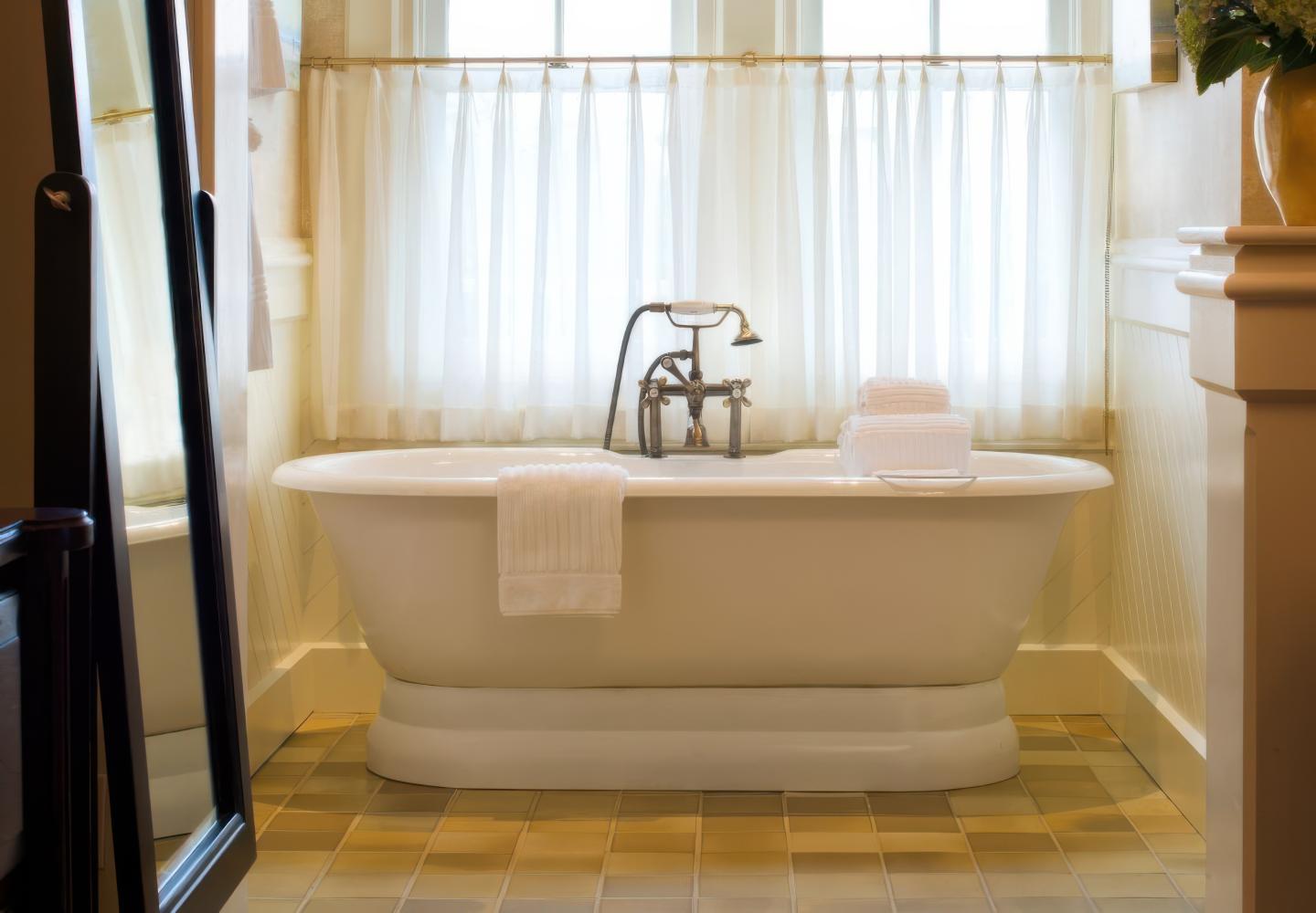 Freestanding bathtub with towels, in a sunlit bathroom.