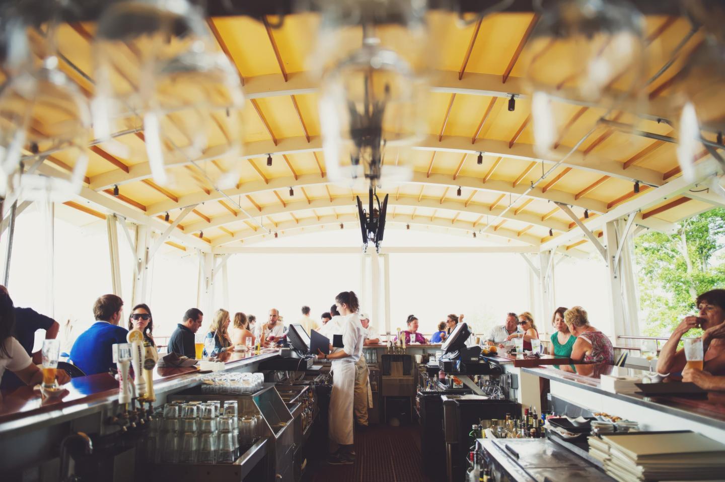 Outdoor bar with people socializing under a wooden canopy.