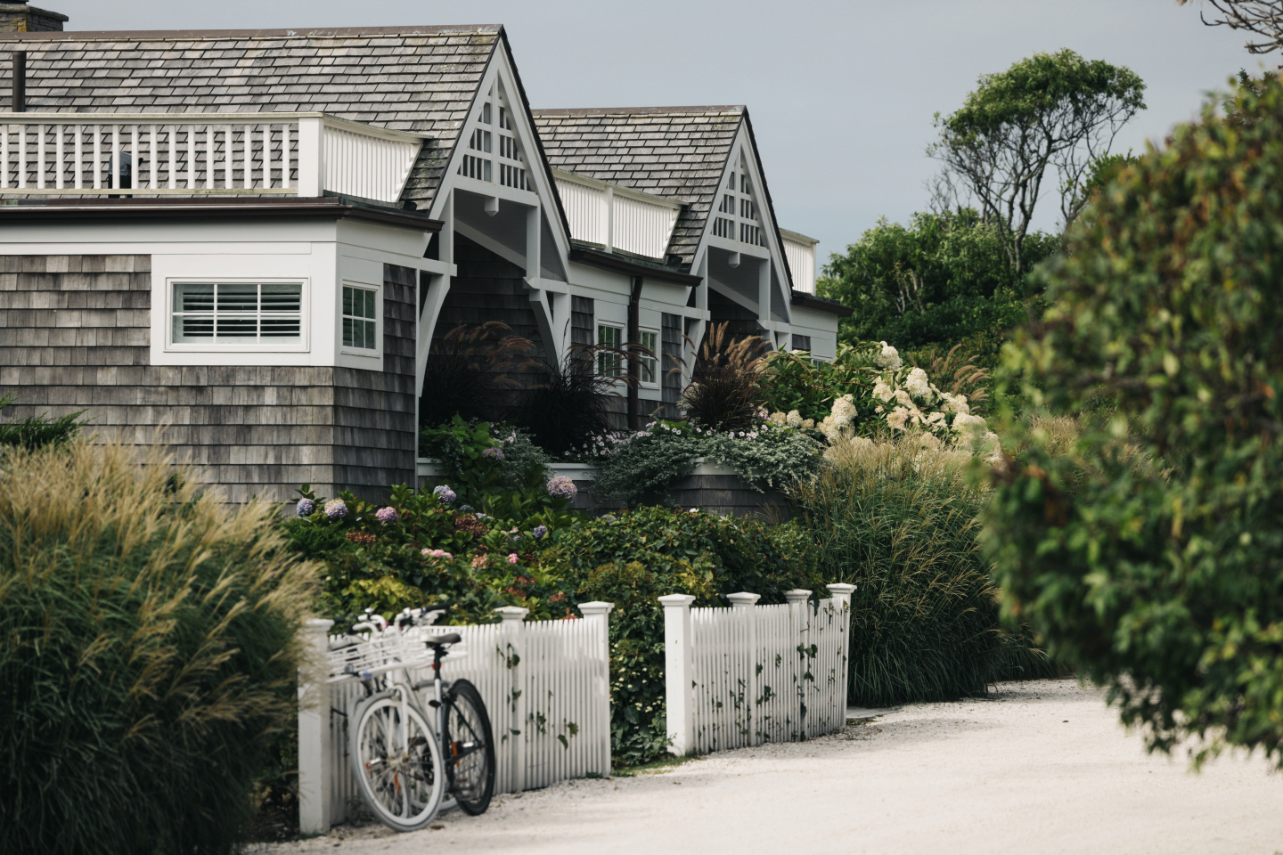 Cottages with shingled roofs, garden, and two white bikes on a sandy path.