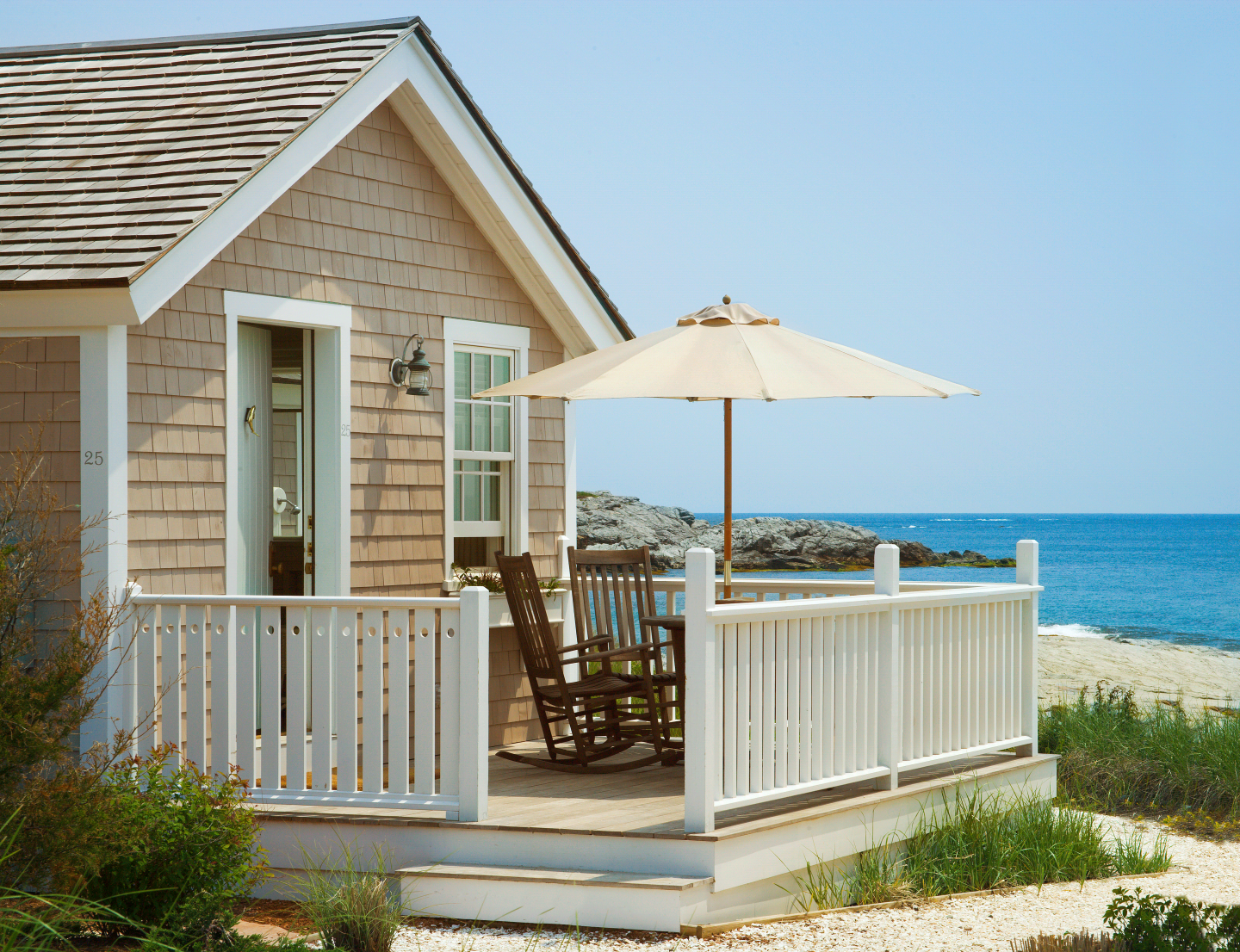 Small beach house porch with chairs, umbrella, and ocean view.