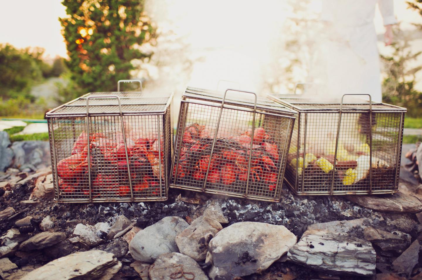 Seafood and corn steaming in wire baskets over an outdoor fire.