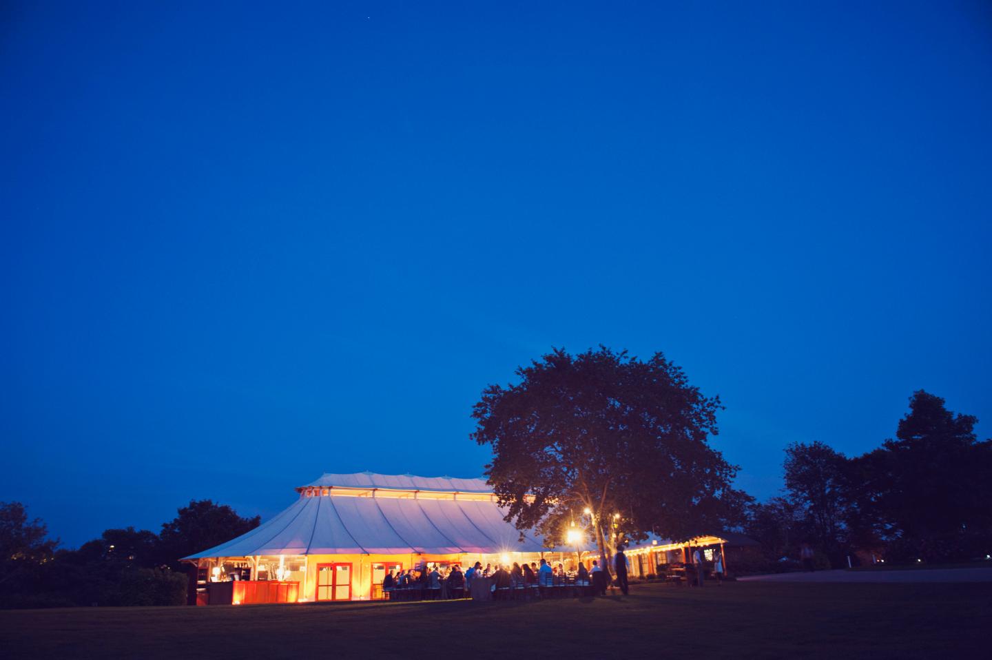 Outdoor event tent with warm lights under a deep blue evening sky.