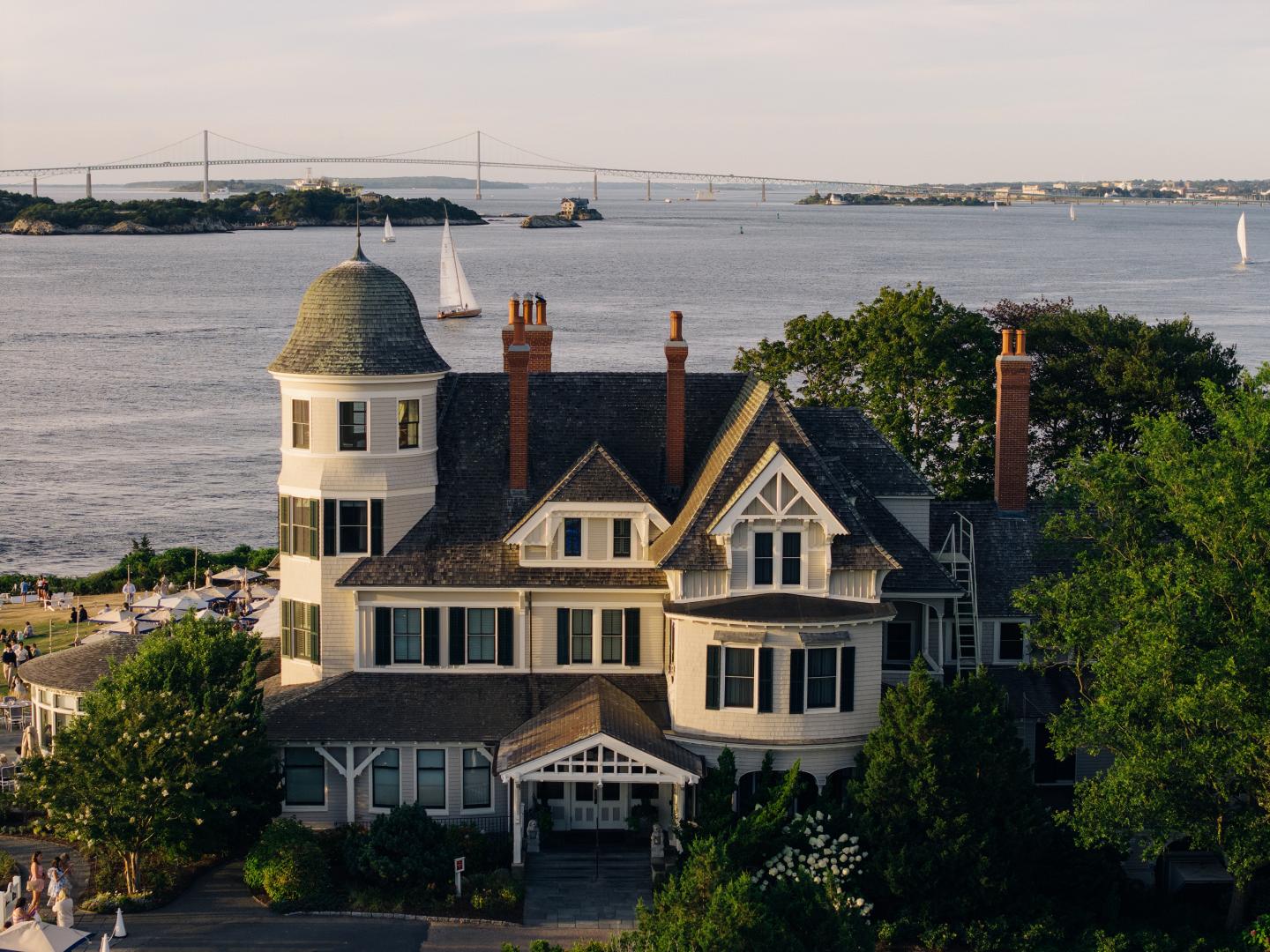 Large house by the sea with a tower, surrounded by trees under a clear sky.