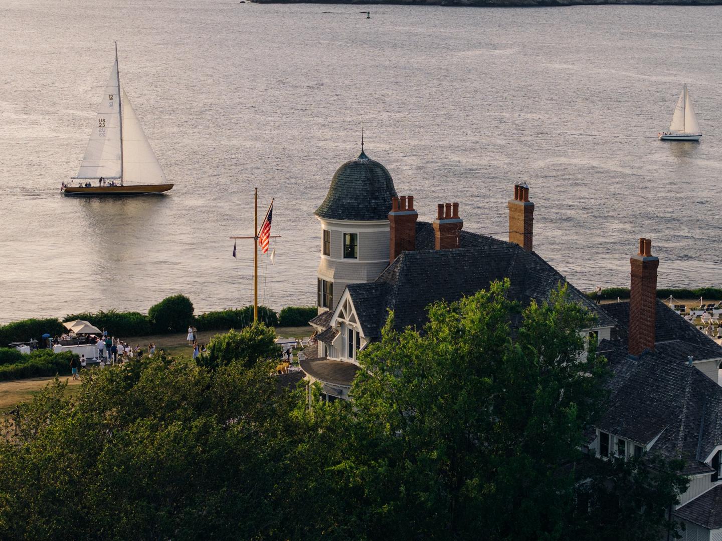 Coastal view with sailboats and a grand house by the water.