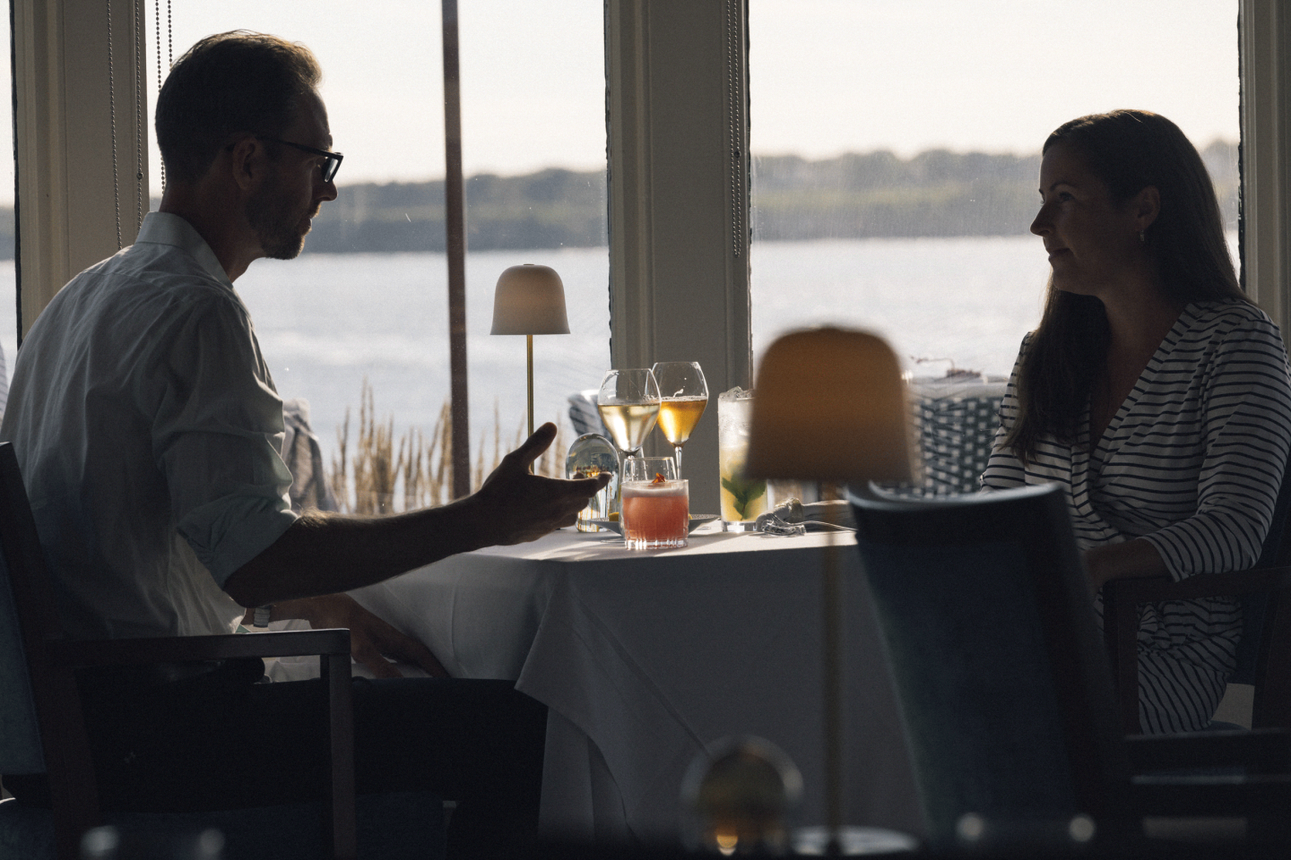 Couple dining at a table by a window overlooking water.