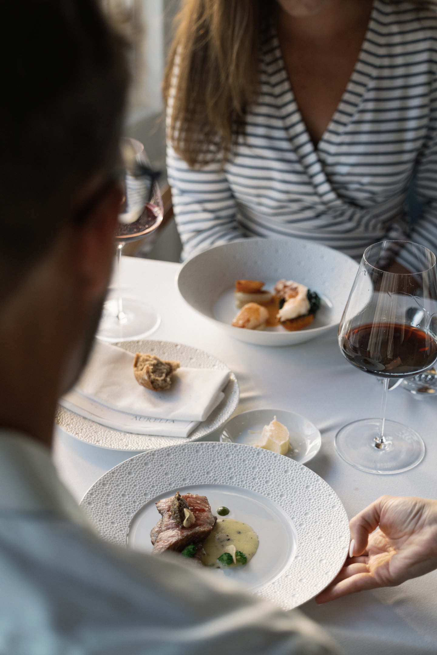 Dining table with two people and plates of gourmet food.