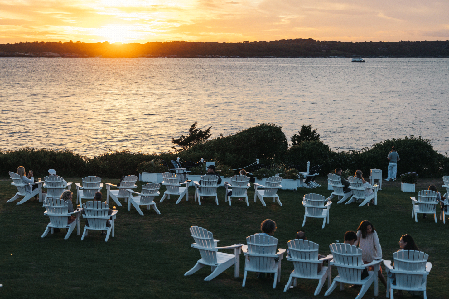 White chairs on a lawn facing a sunset over the water.