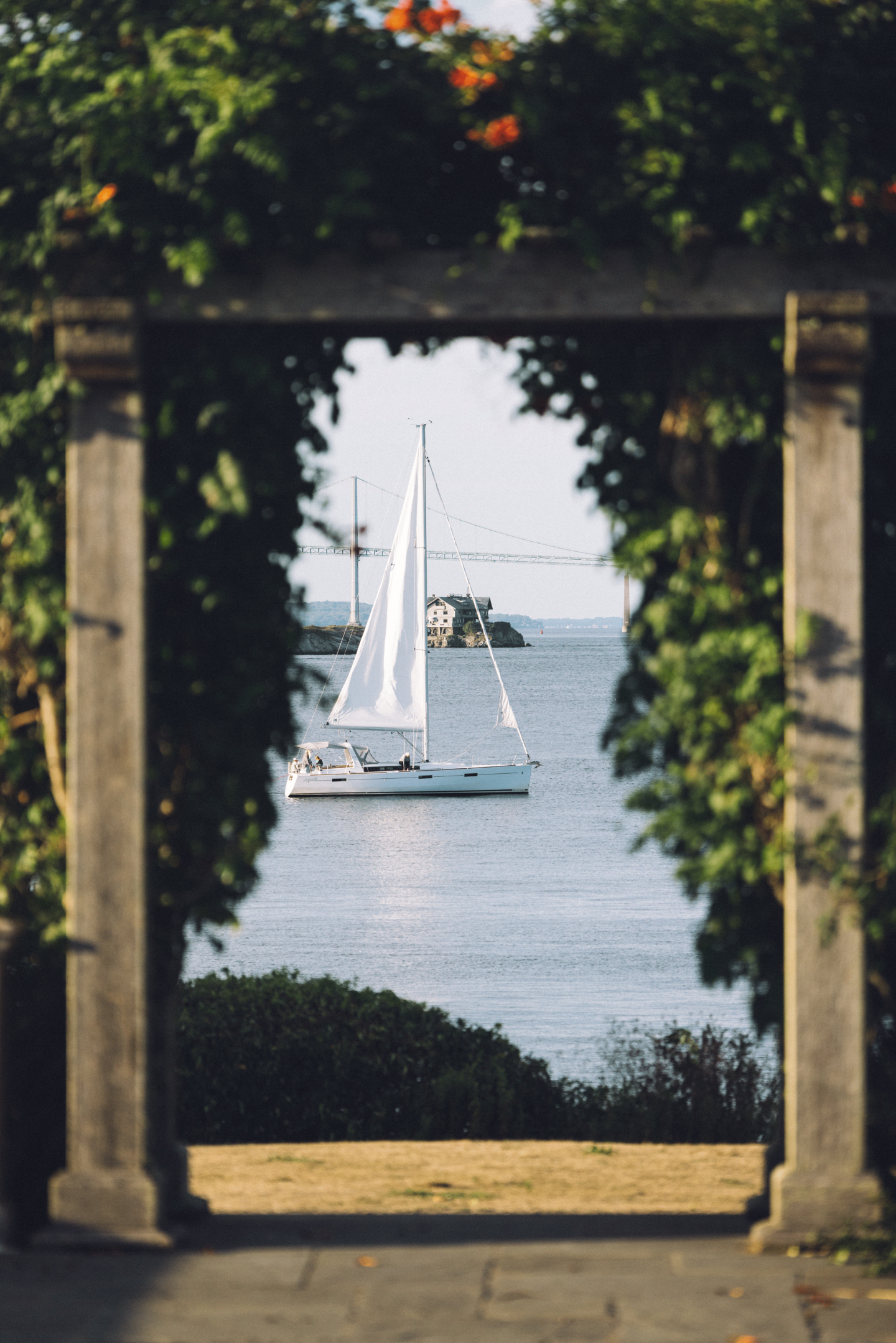 Sailboat on a calm sea, framed by a leafy archway.