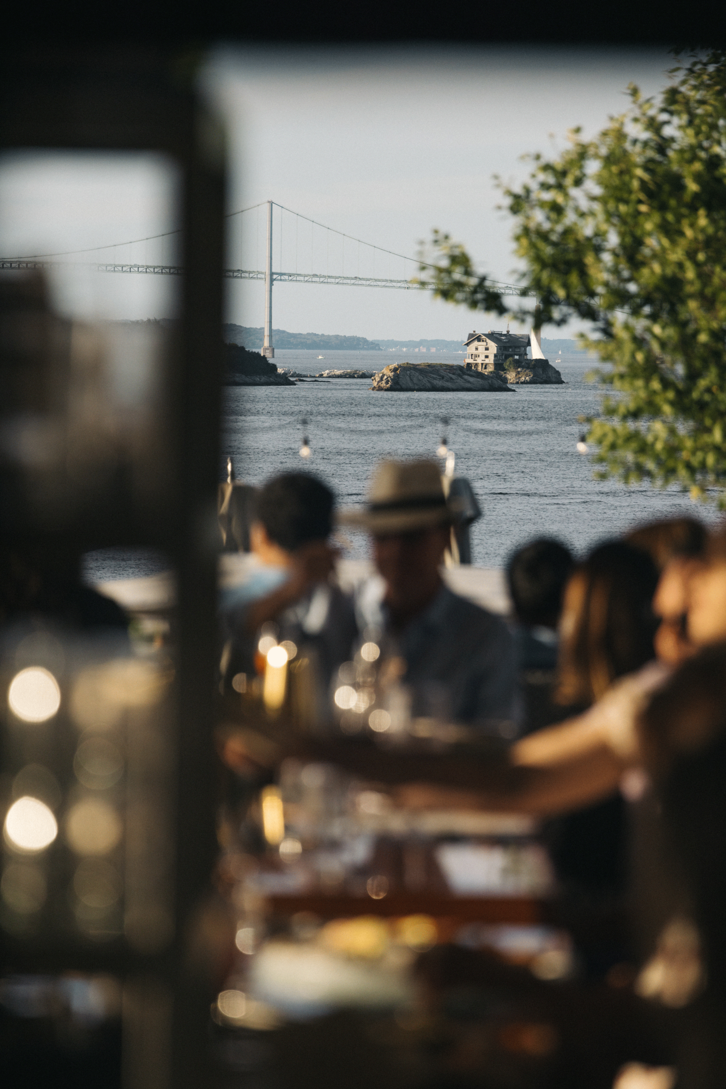 Outdoors dining, blurred people in foreground, water and bridge in distance.