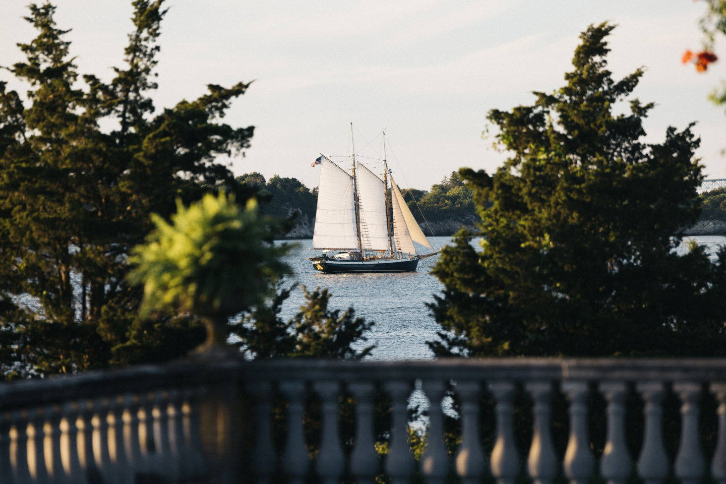 Sailing ship viewed through trees and a stone railing.