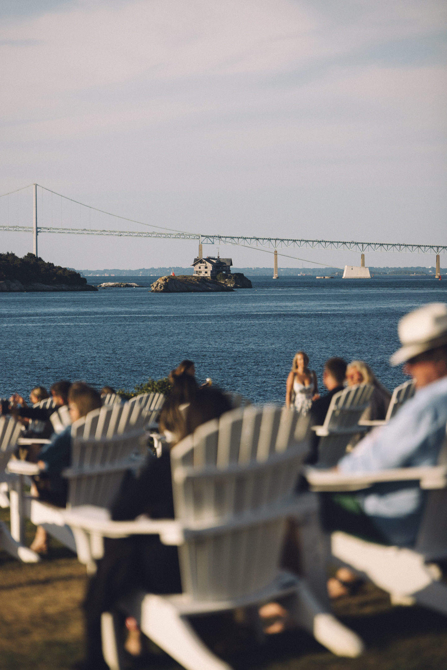 Chairs on a lawn by water, people resting under a sunny sky.