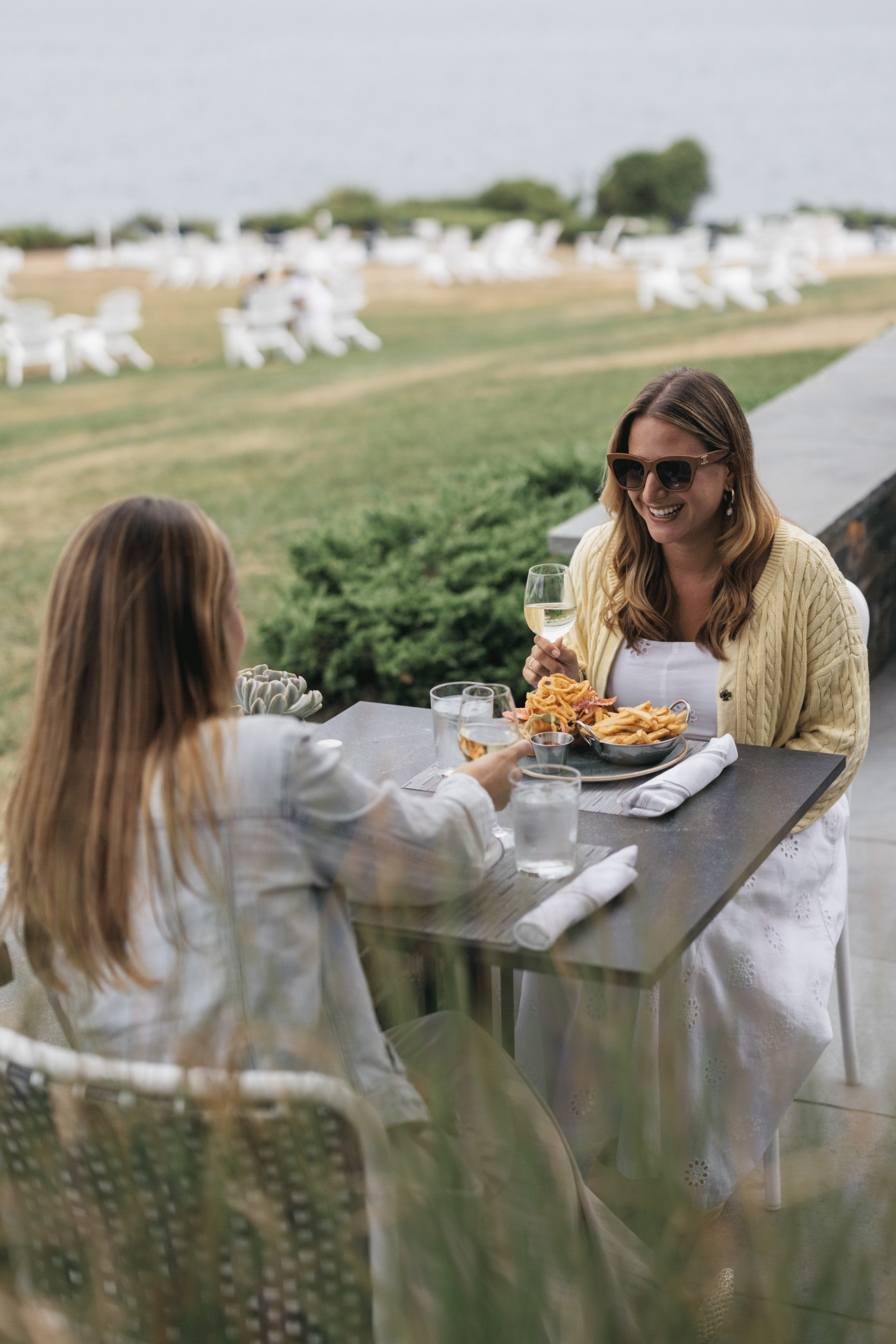 Two people dining outdoors by a grassy field and water view.