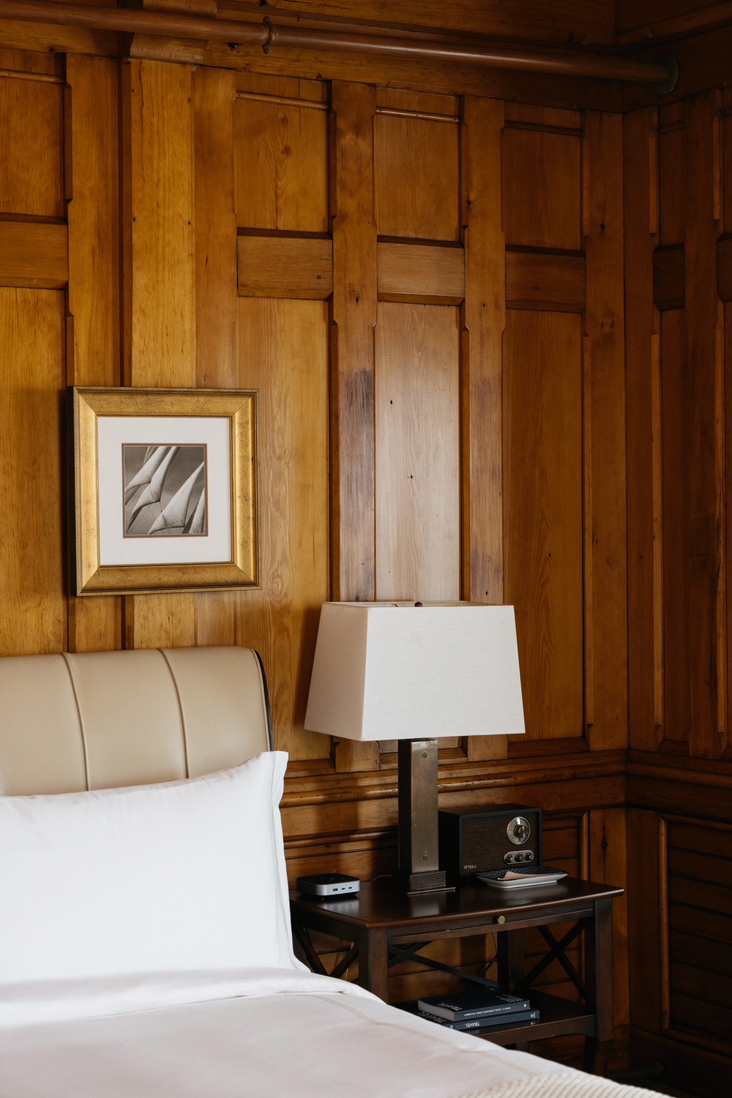 Wood-paneled room with bed, nightstand, lamp, and framed artwork.
