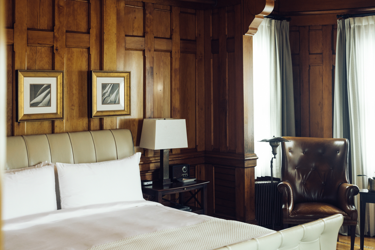 Wood-paneled bedroom with a bed, leather chair, and lamp by the window.