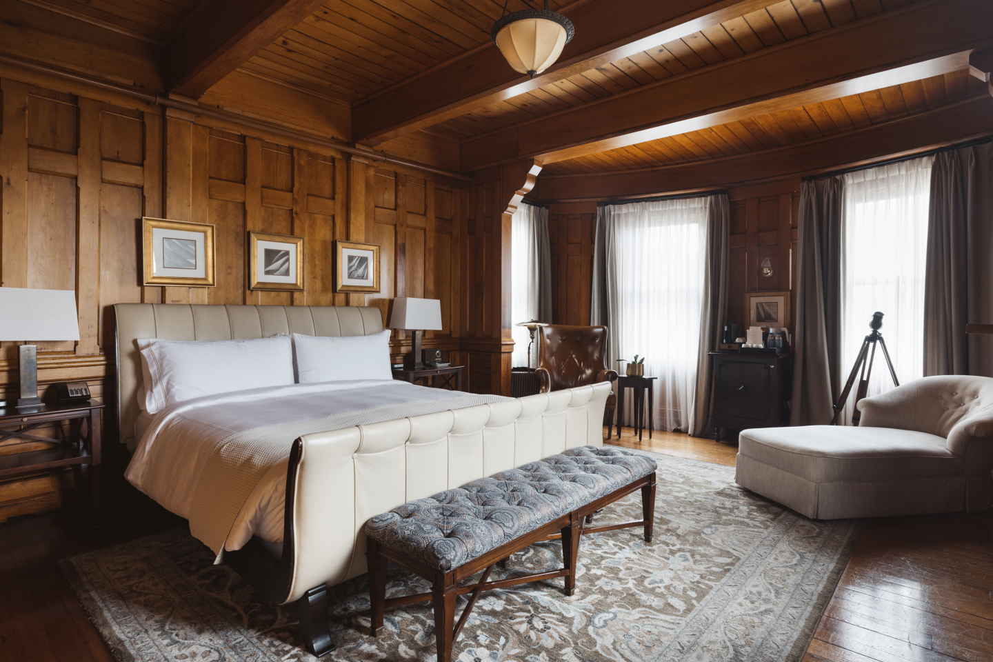Luxurious wooden bedroom with a large bed, bench, and chaise lounge by the window.