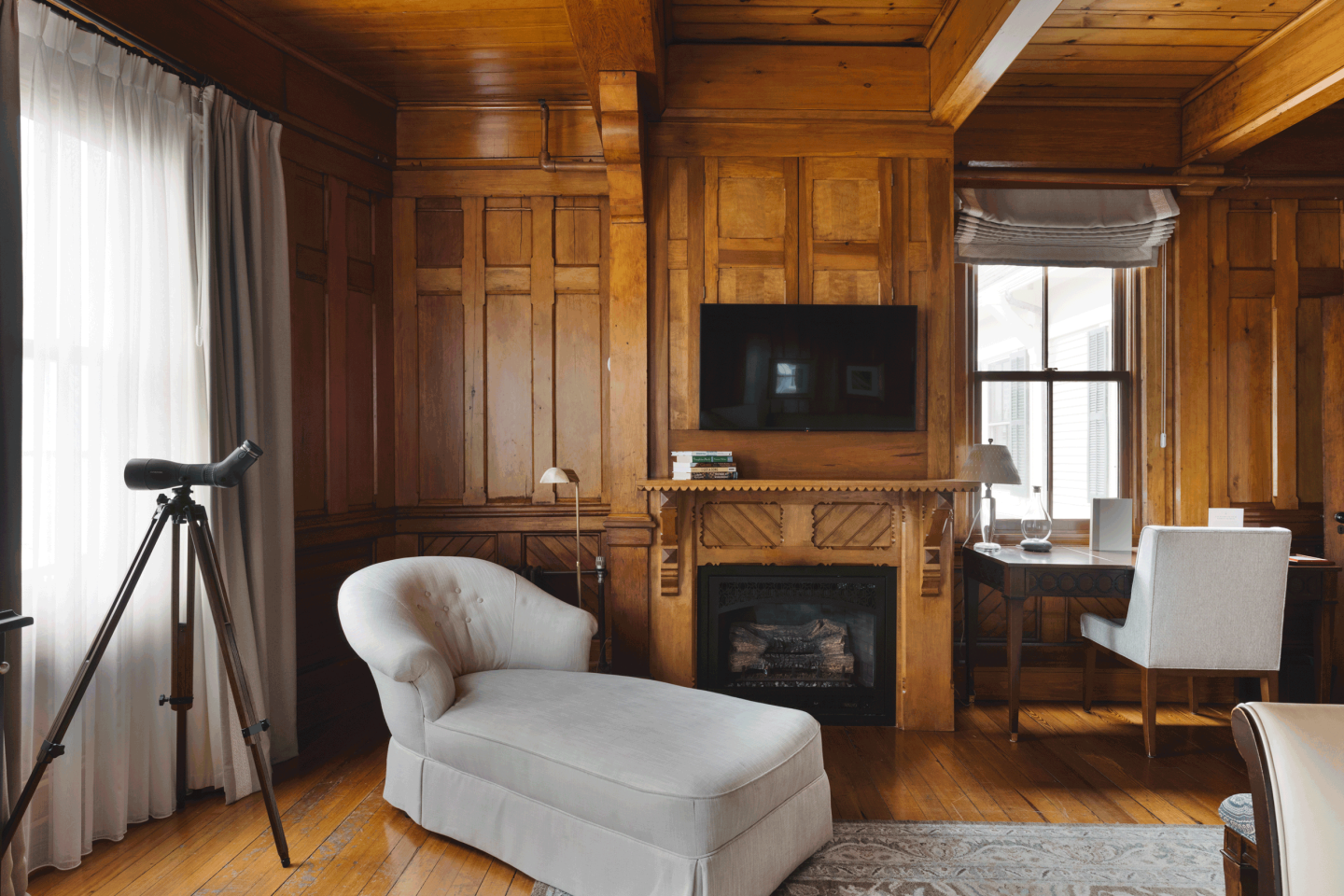 Elegant room with wood paneling, chaise lounge, telescope, and a small desk near a window.