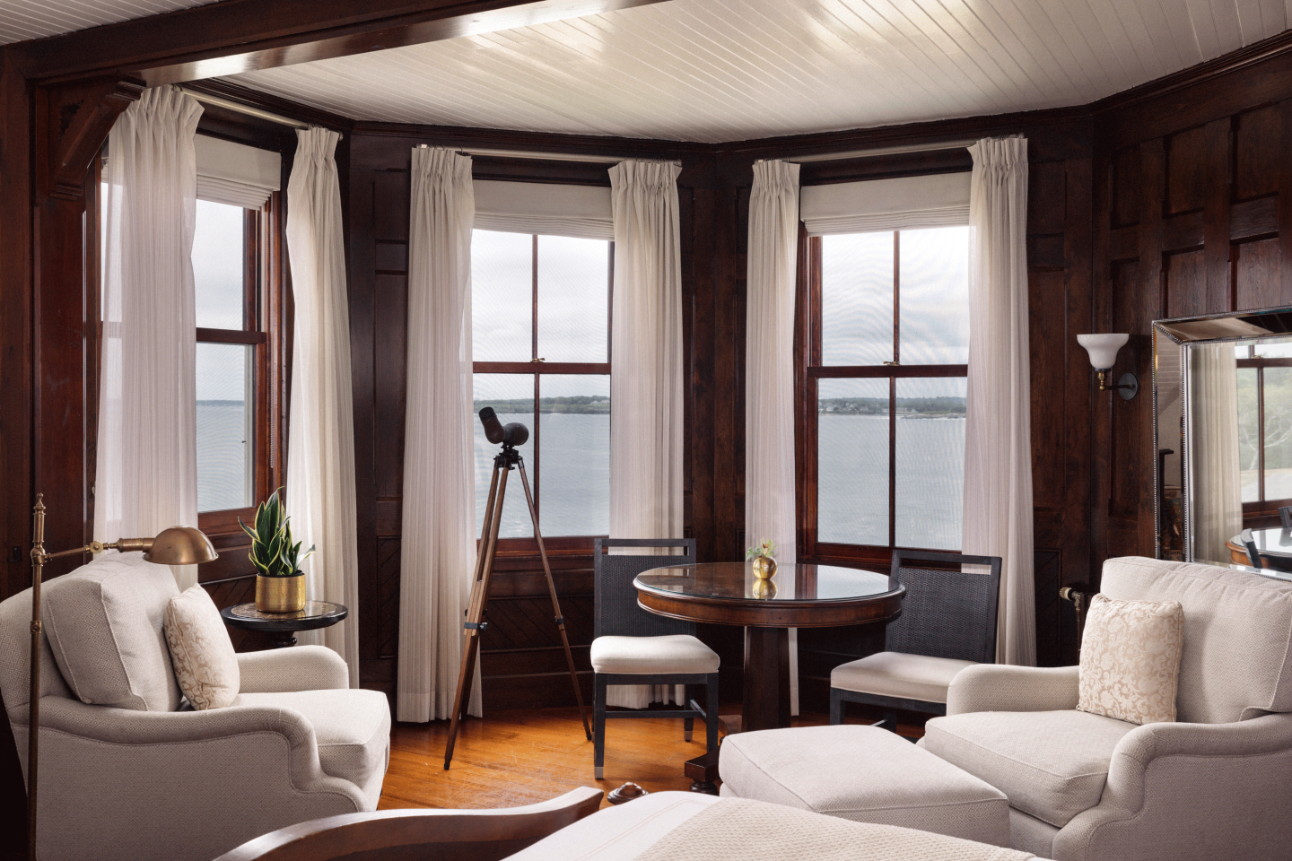 Cozy room with bay windows, armchairs, and a tripod overlooking a lake.