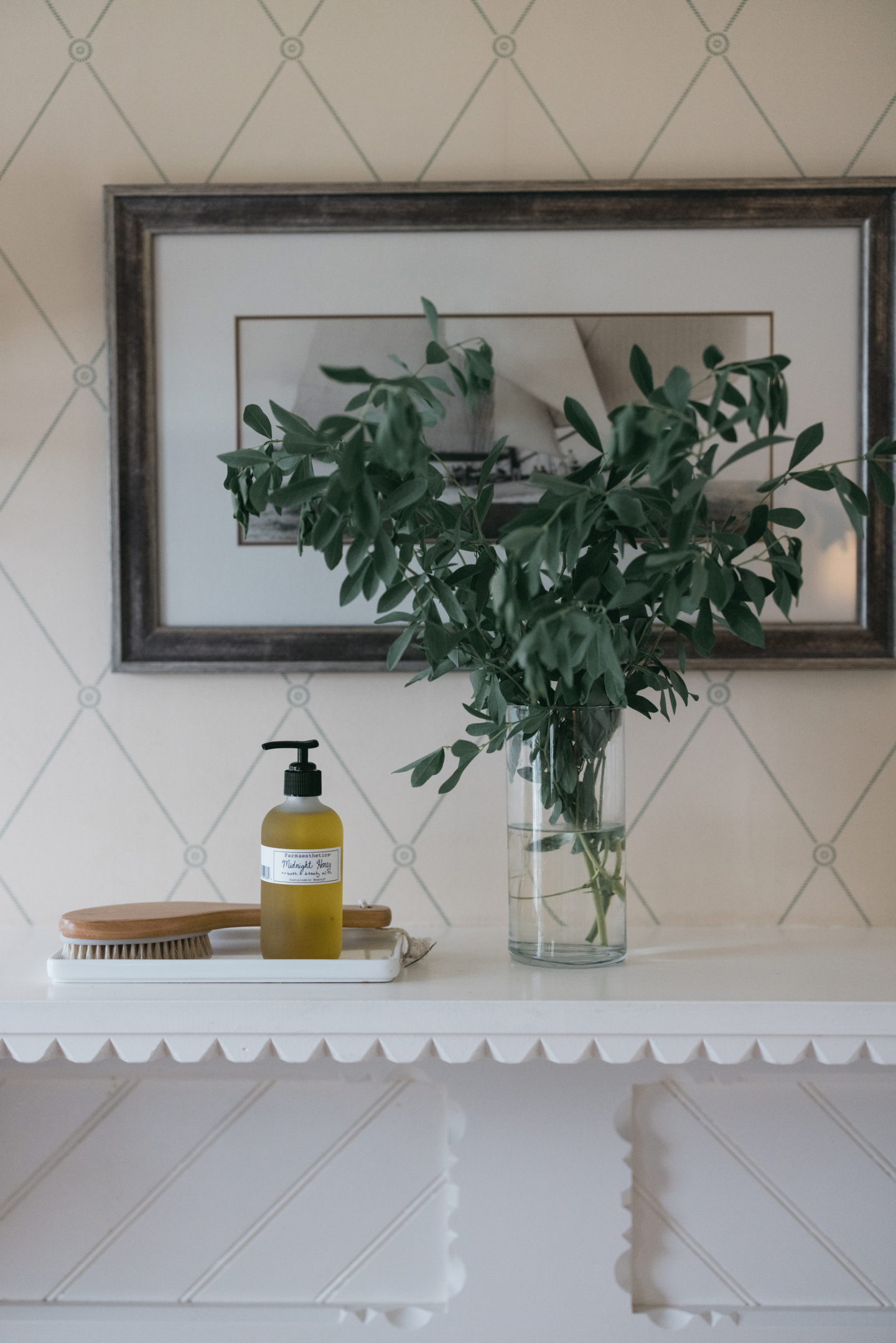Vase with green leaves on a mantel, framed art in background.