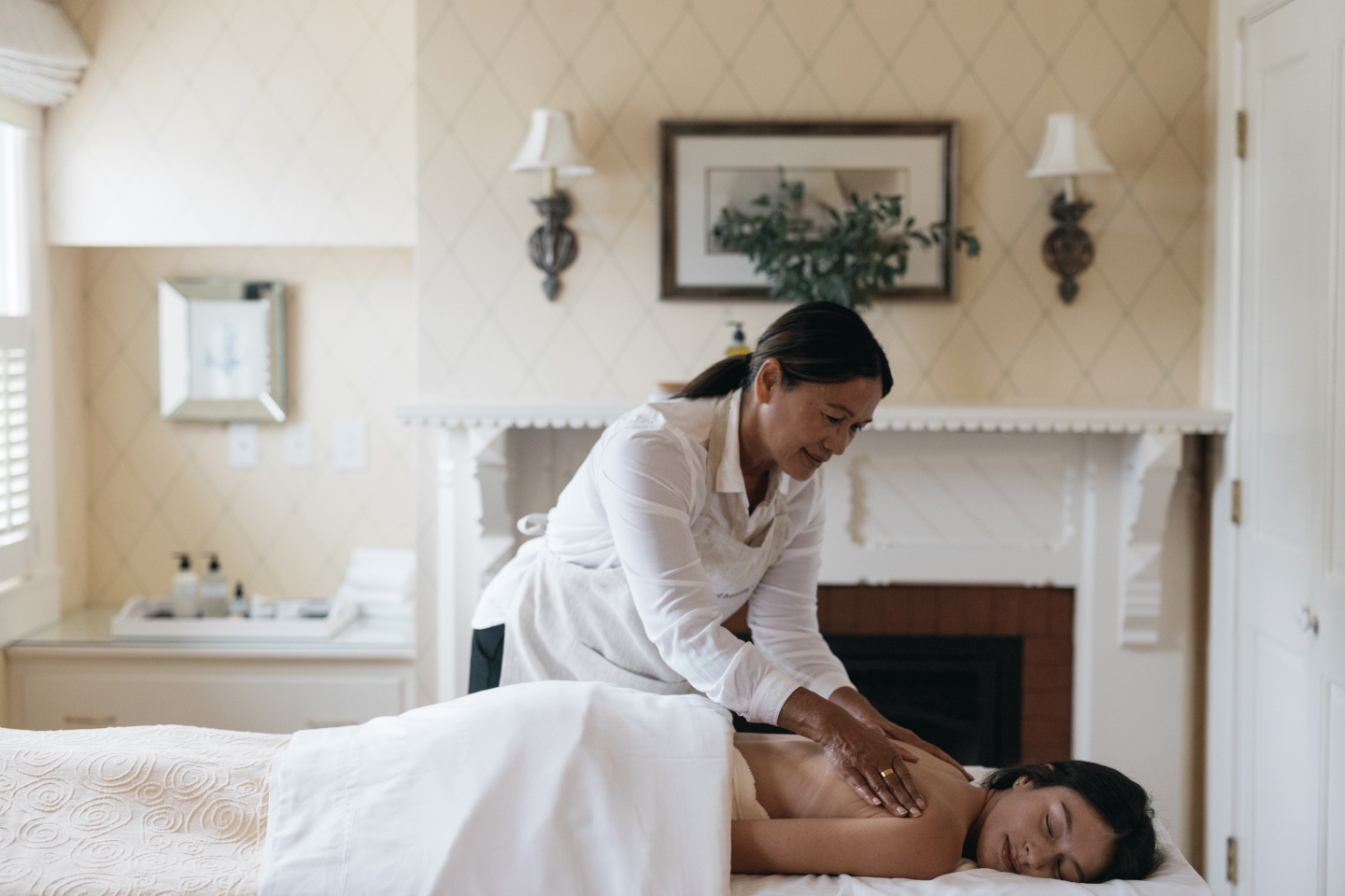 Spa therapist giving a massage in a cozy room with beige walls.