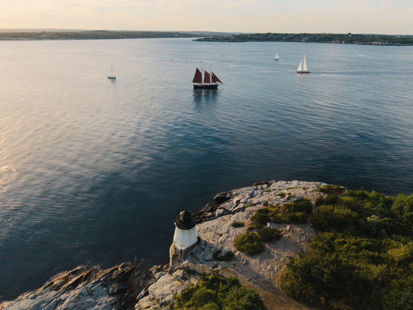 Aerial view of a lighthouse by the coast with sailboats on the water.