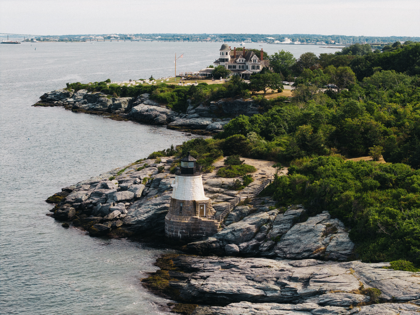 Coastal lighthouse surrounded by greenery and rocks.