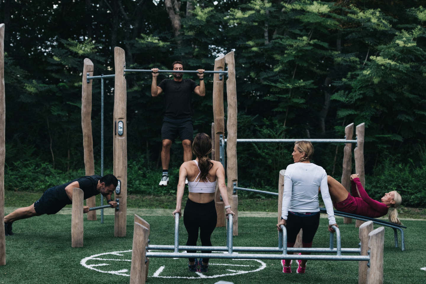 Group exercising at outdoor fitness park with bars, surrounded by trees.
