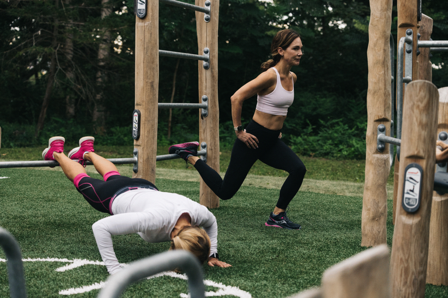 Two women exercising outdoors with gym equipment on grass.