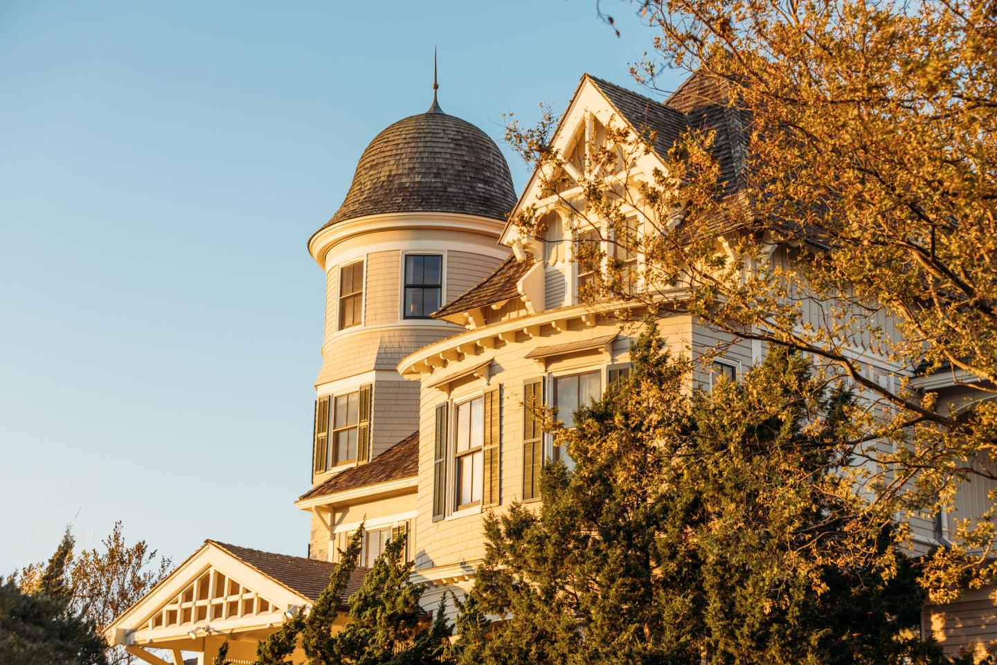Victorian house with a turret, surrounded by autumn trees.
