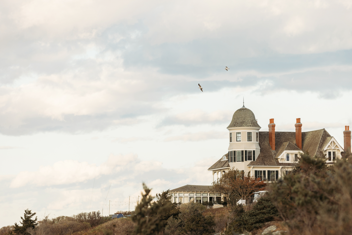 Elegant seaside house with turret, under a cloudy sky.