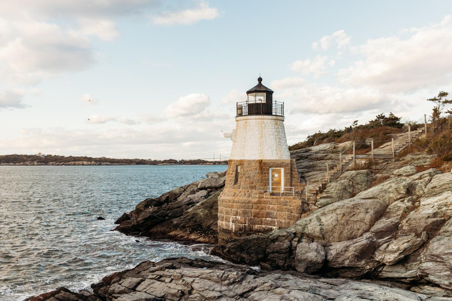 Lighthouse on rocky coastline under a partly cloudy sky.