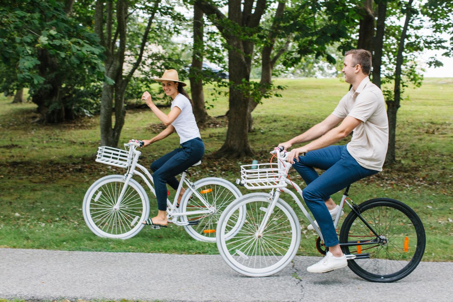 Two people riding white bicycles in a park, surrounded by trees.