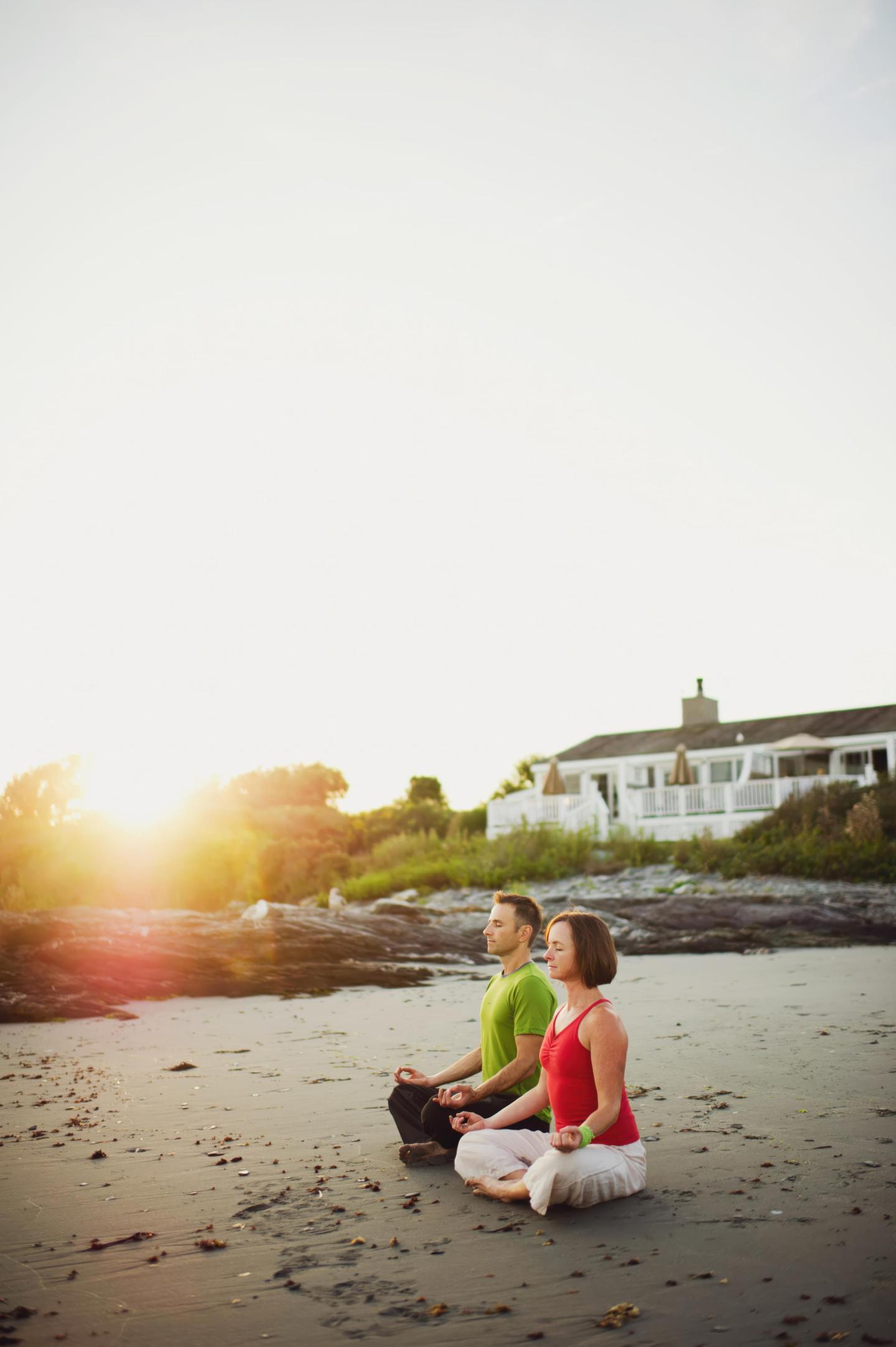 Two people meditating on a beach at sunrise.