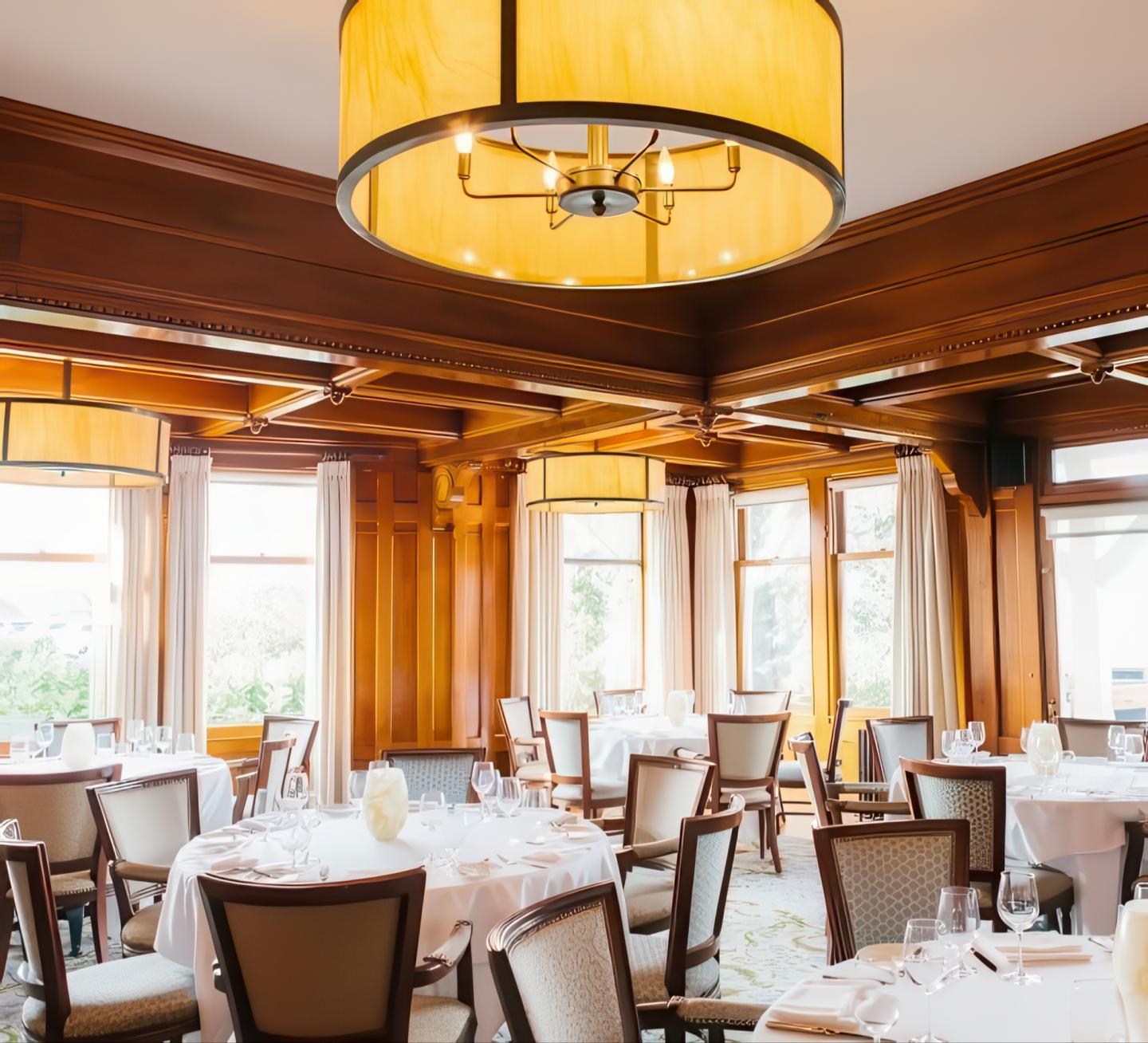 Elegant dining room with round tables, white tablecloths, and large hanging light fixtures.