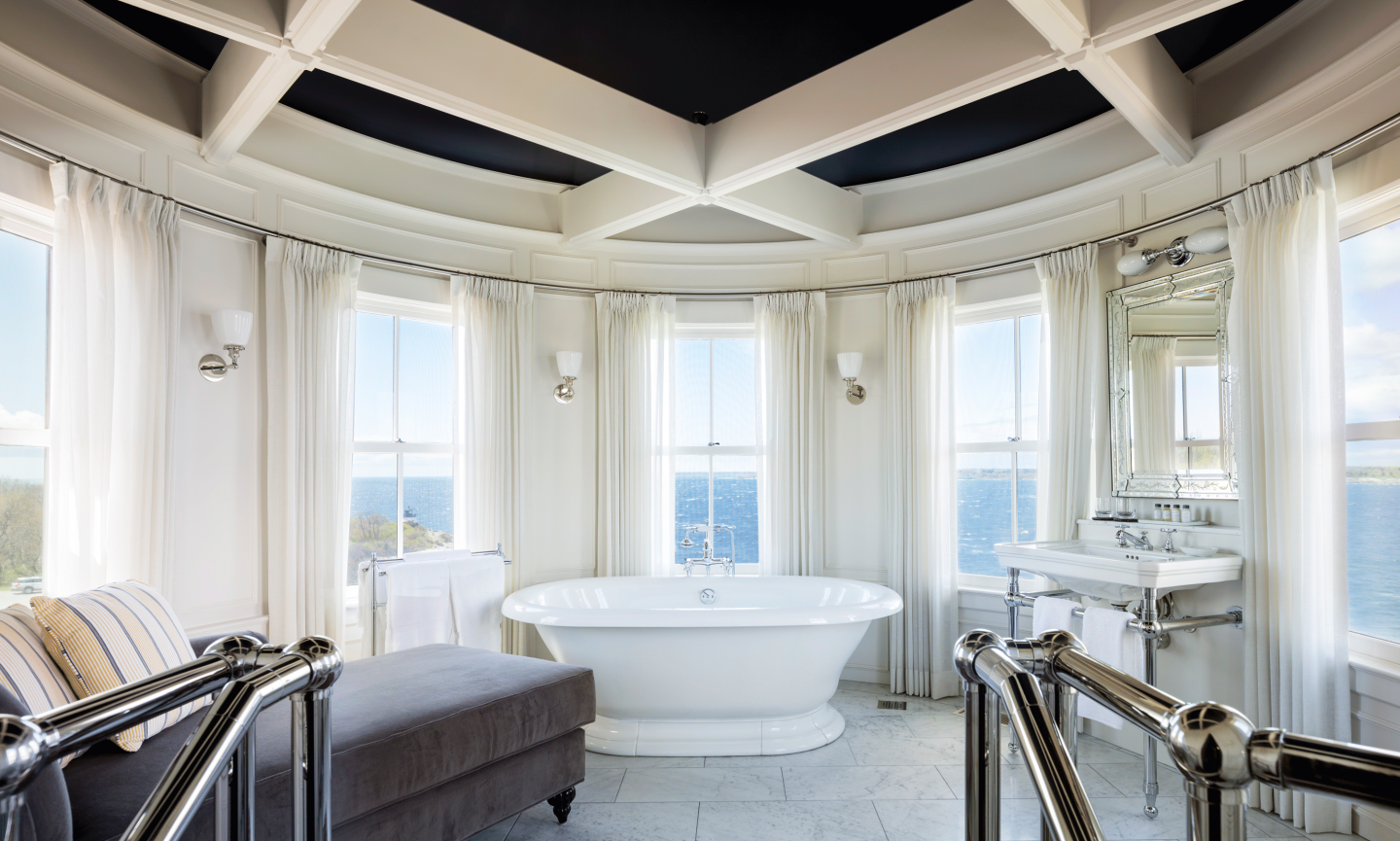 Bright bathroom with a central bathtub, windows, and white curtains.