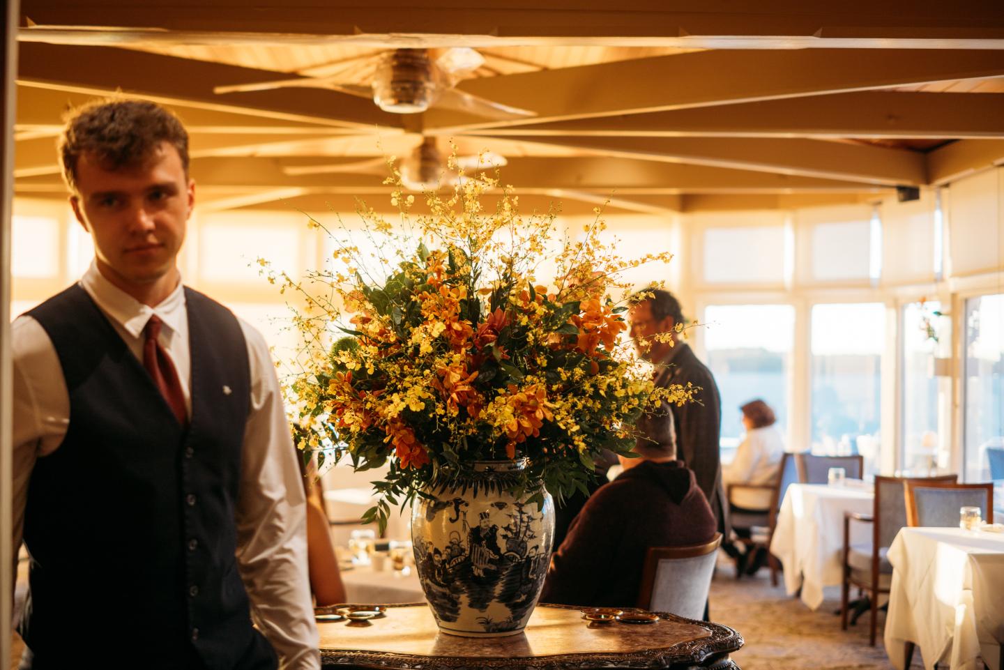 Restaurant with a waiter, large floral centerpiece, and diners in the background.
