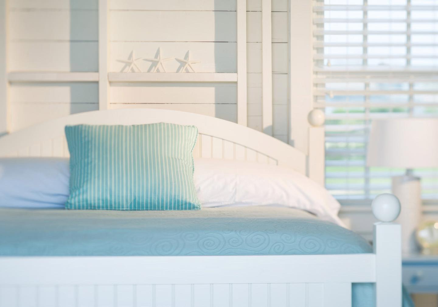 White bed with blue pillow, coastal decor, and soft natural light.