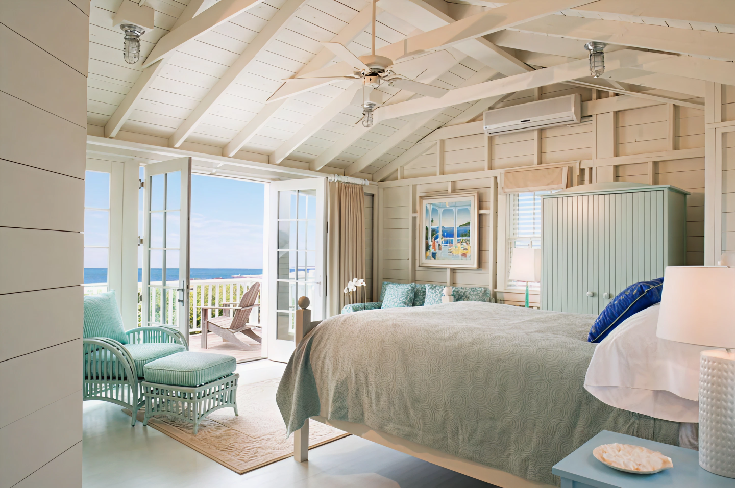 Bright beach-themed bedroom with ocean view, cozy seating, and subtle pastel decor.