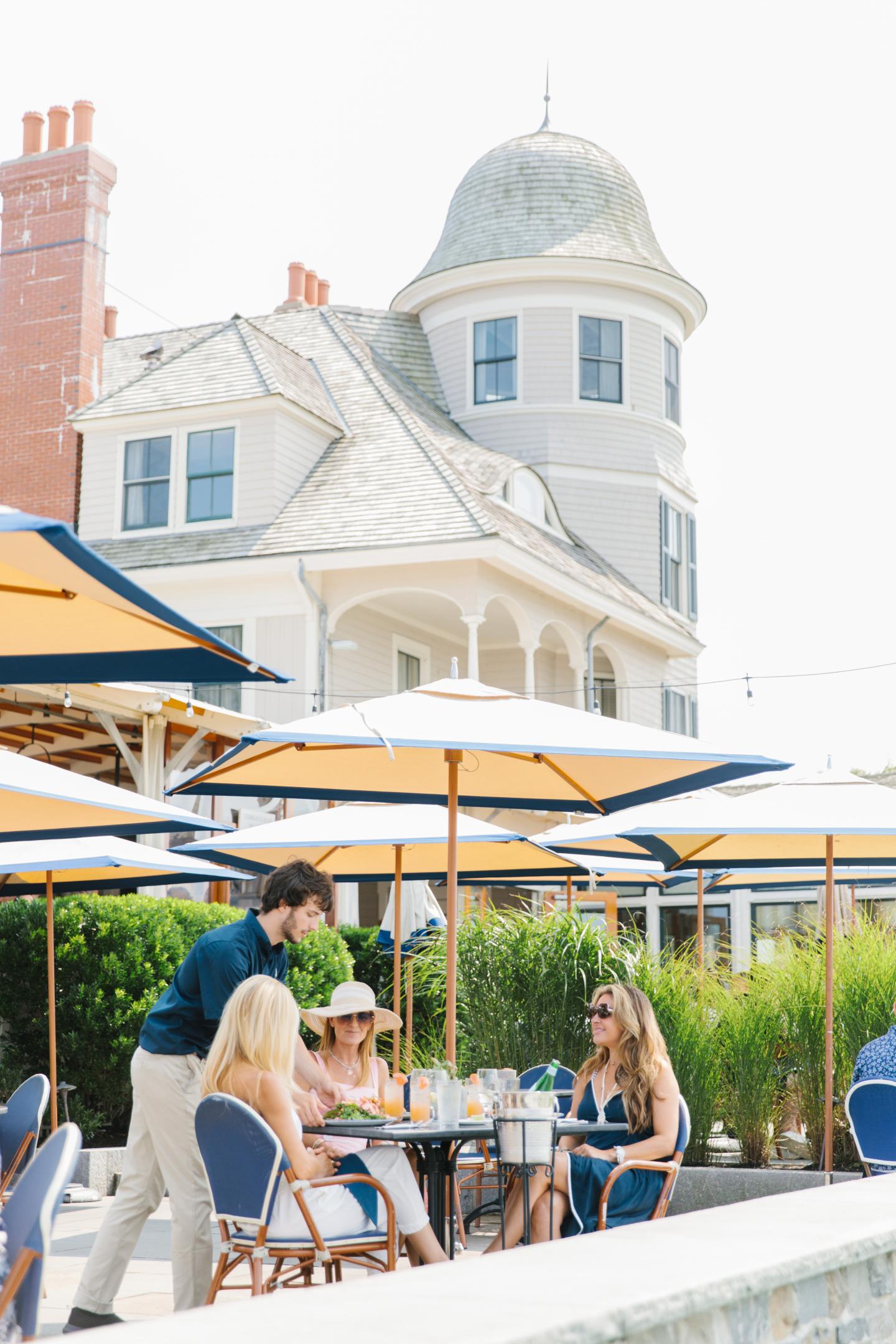 Outdoor café with people seated under umbrellas, historic building in background.