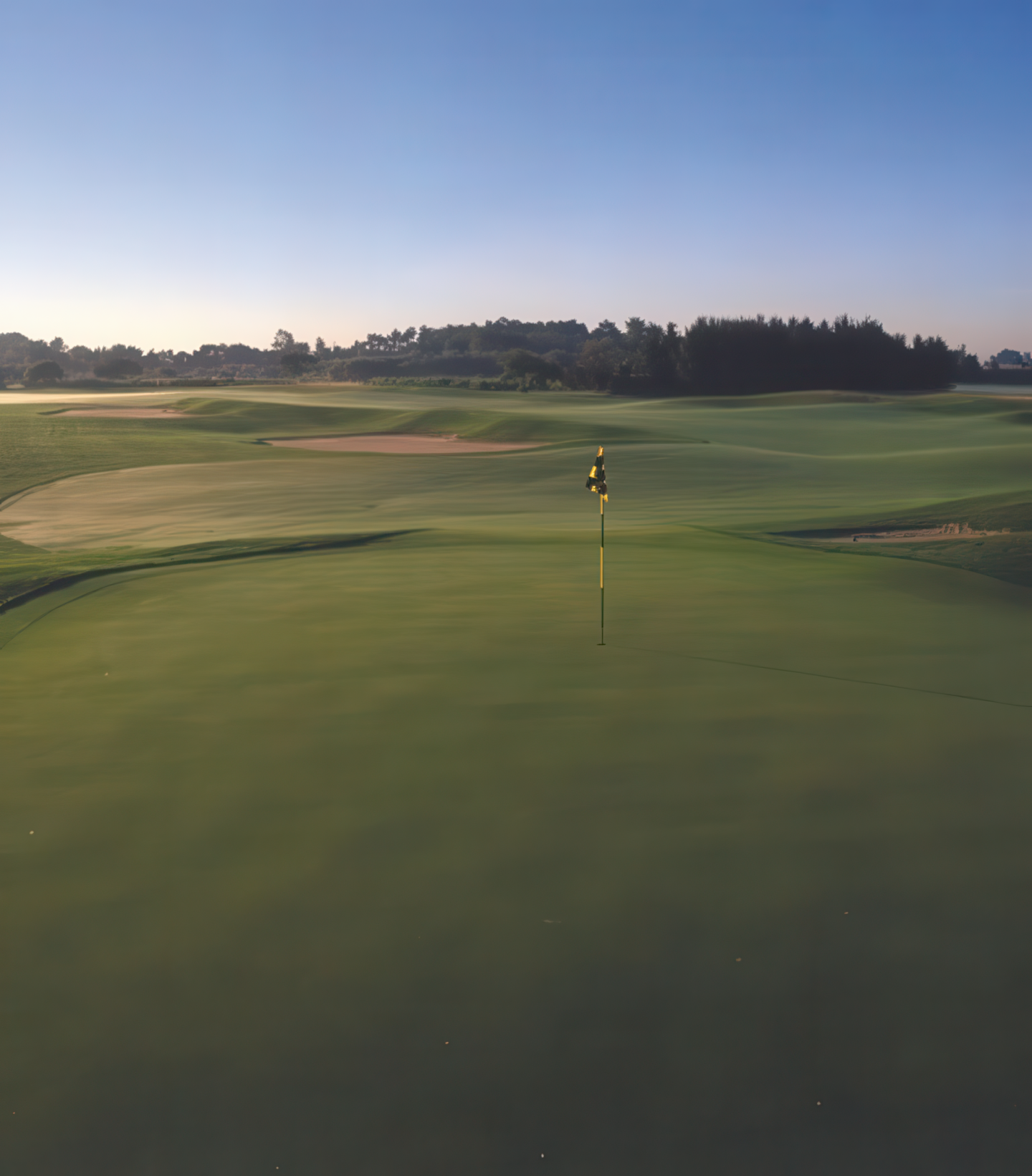 Golf course green under a clear blue sky at sunset.