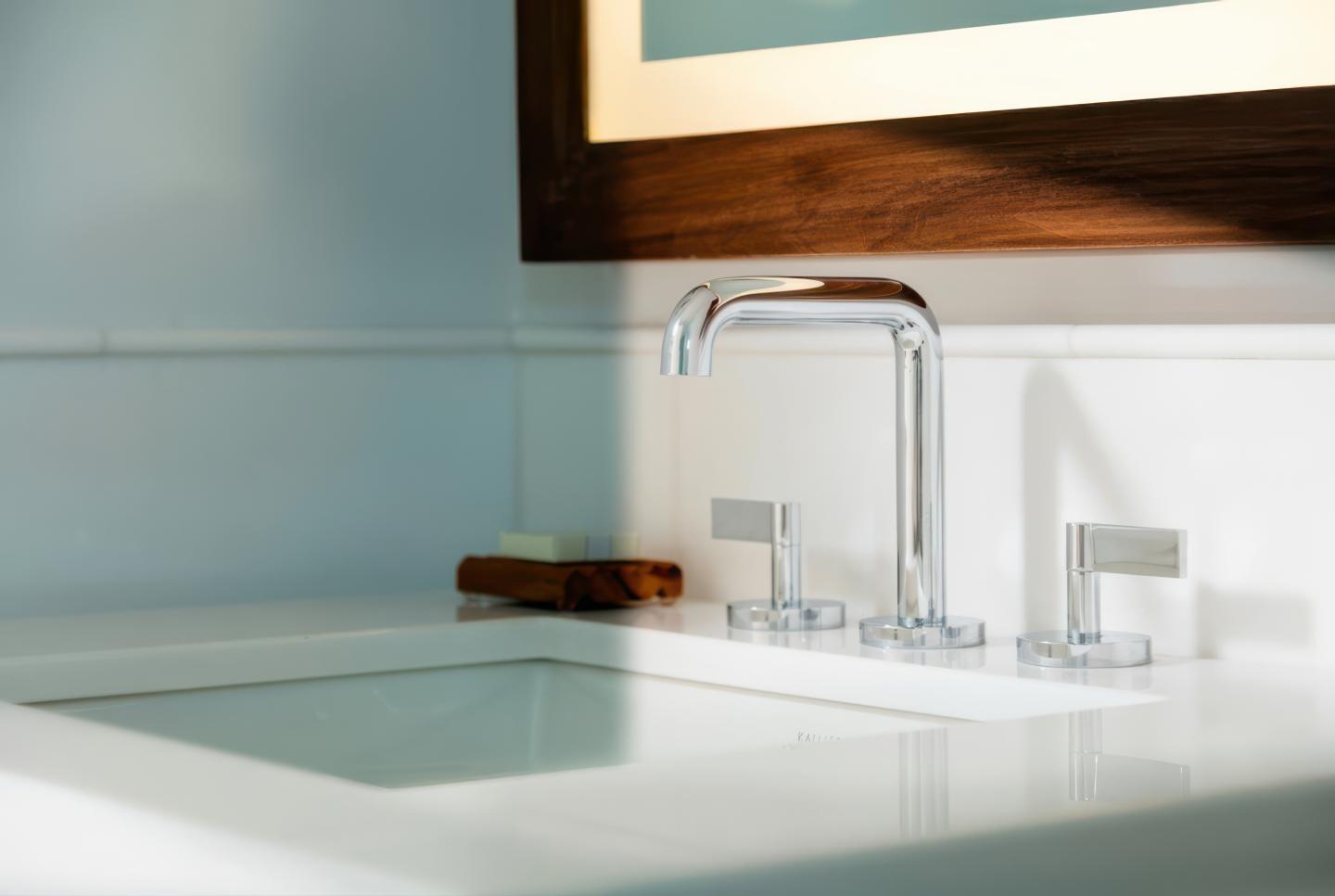 Modern bathroom sink with chrome faucet and wooden-framed mirror.