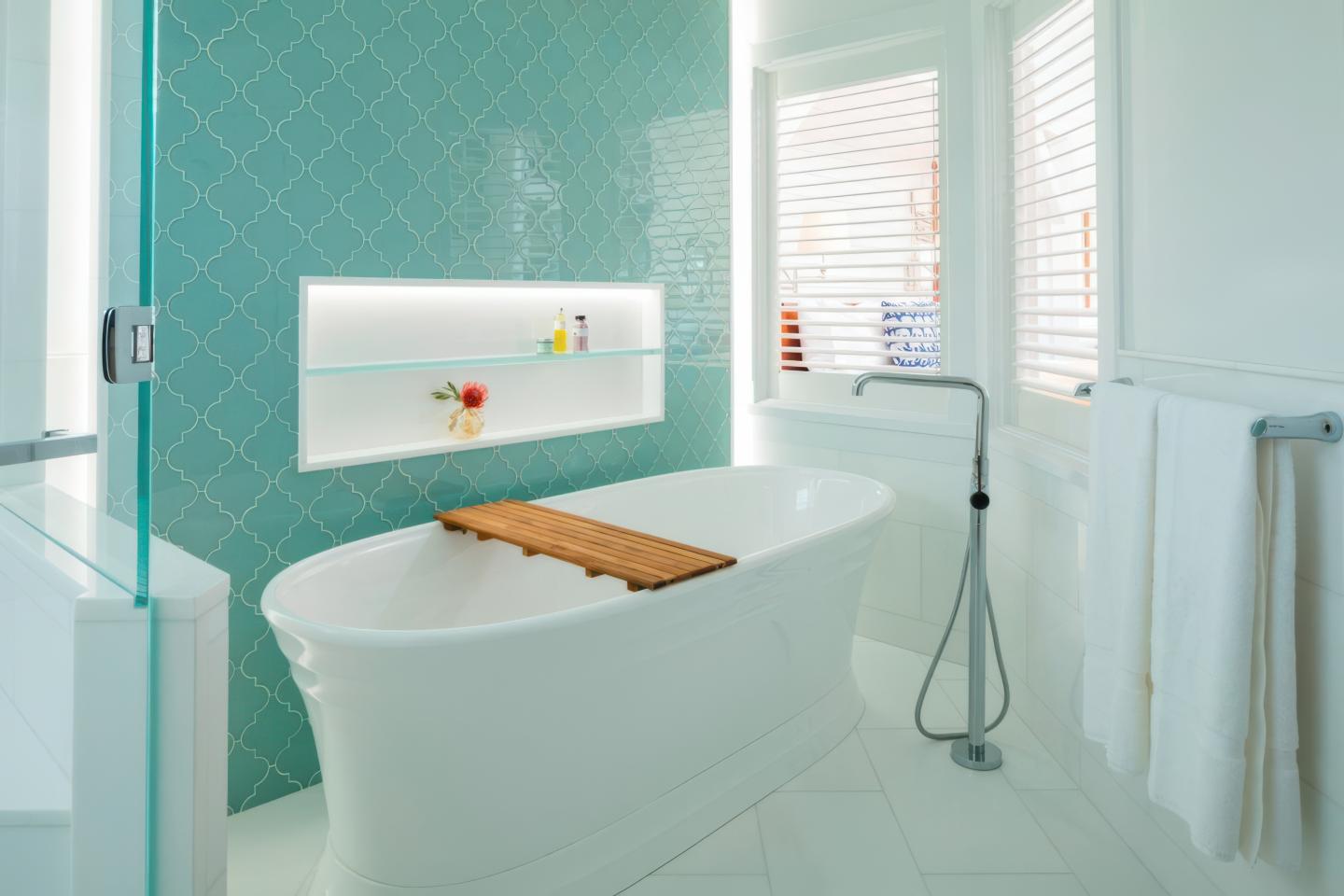 Bright bathroom with a white tub, teal tiled wall, and natural light.