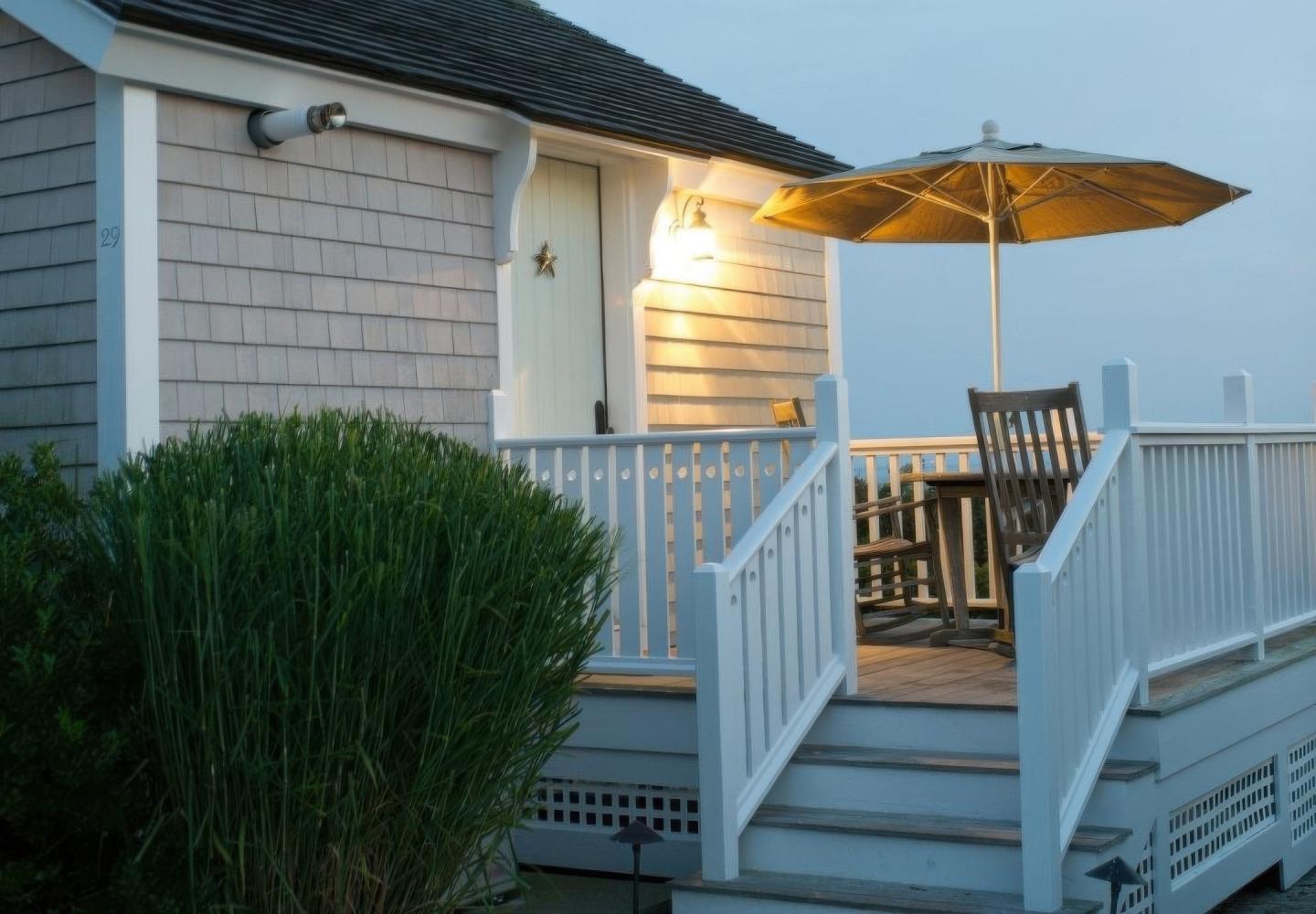 Cozy porch with wooden chairs, umbrella, and soft lighting at dusk.