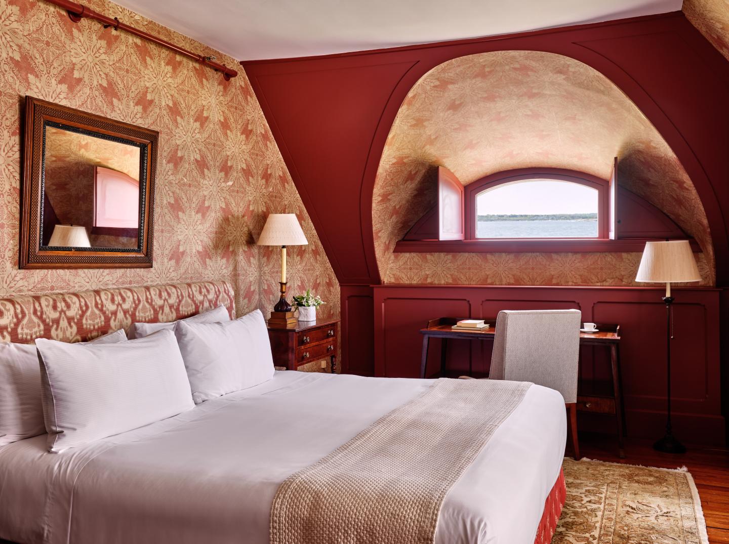 Cozy bedroom with red walls, a large bed, desk, and arched window.