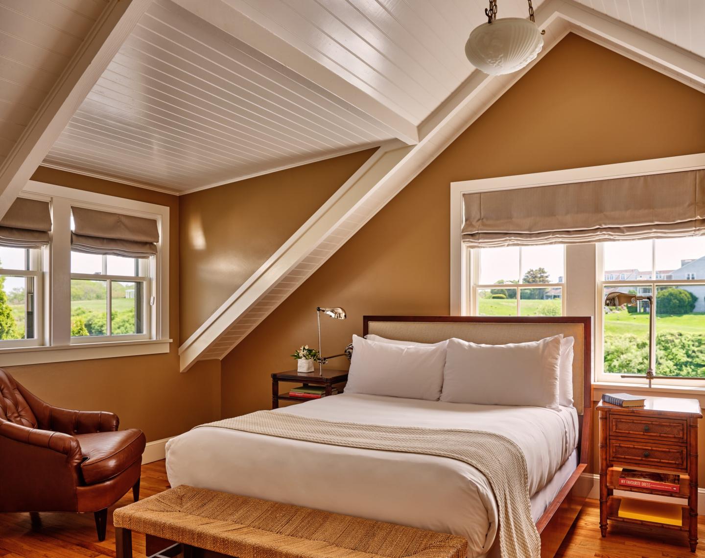 Cozy attic bedroom with sloped ceiling, large bed, and windows showing green landscape.