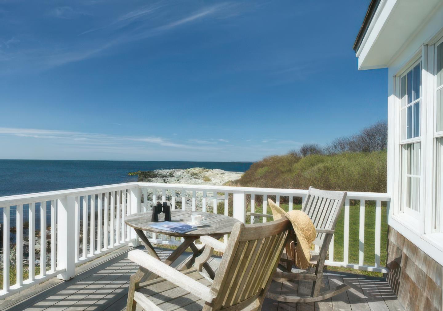 Cozy seaside deck with wooden chairs and a sea view under clear blue skies.