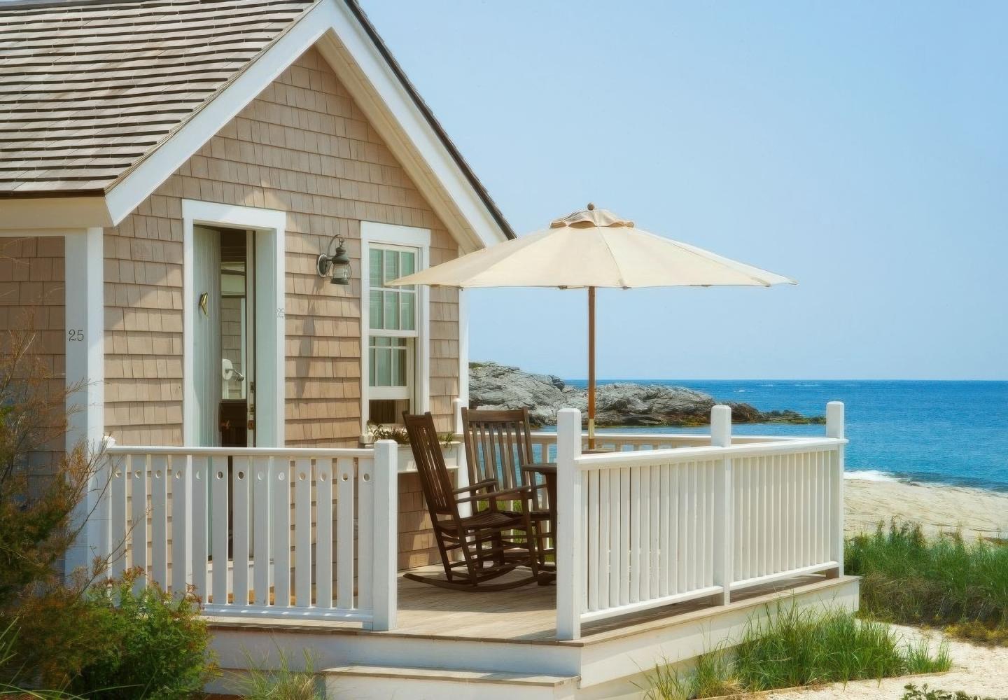Beach house with porch, rocking chairs, and umbrella overlooking the ocean.