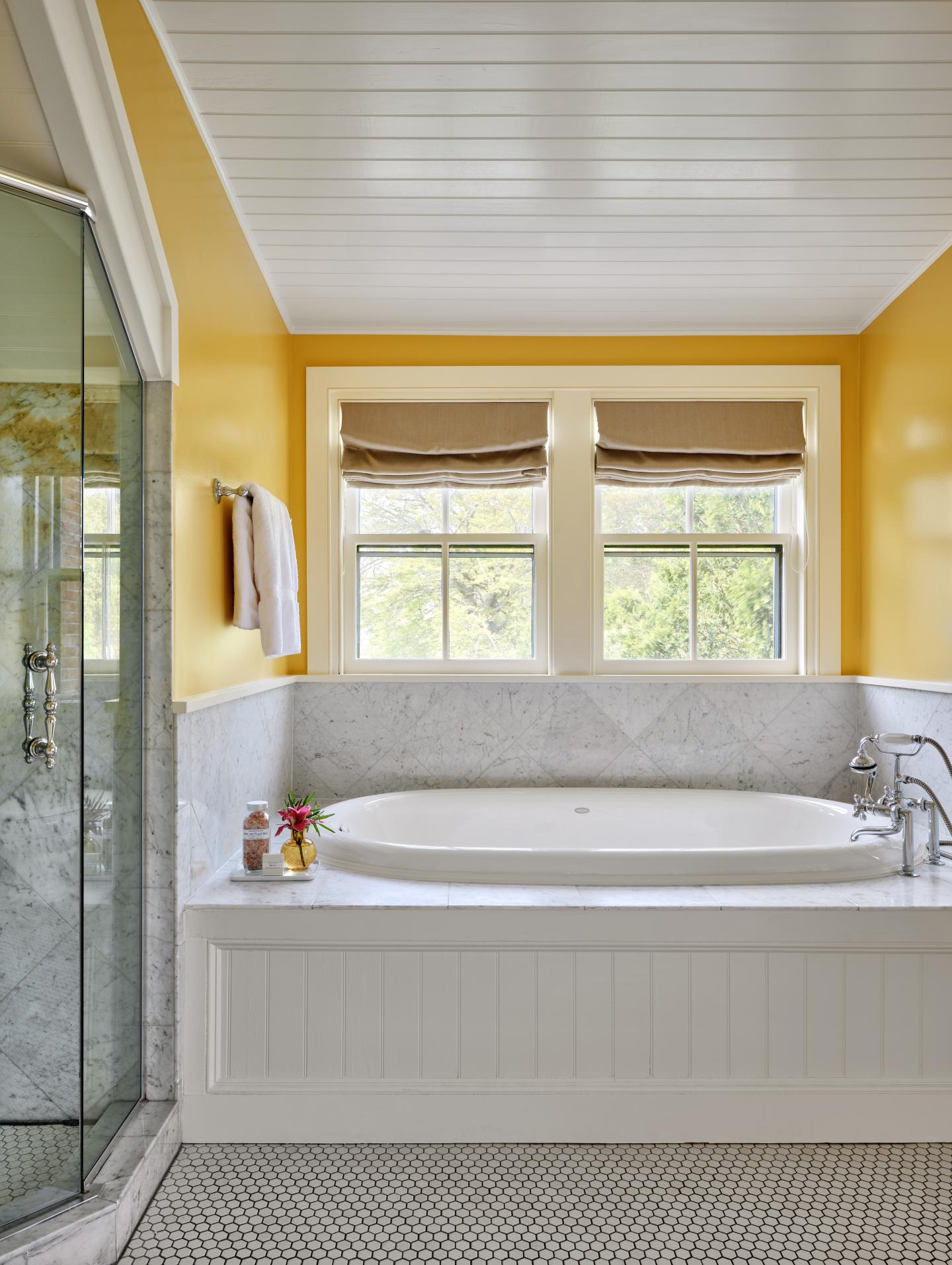 Cozy bathroom with a white bathtub, yellow walls, and two windows.