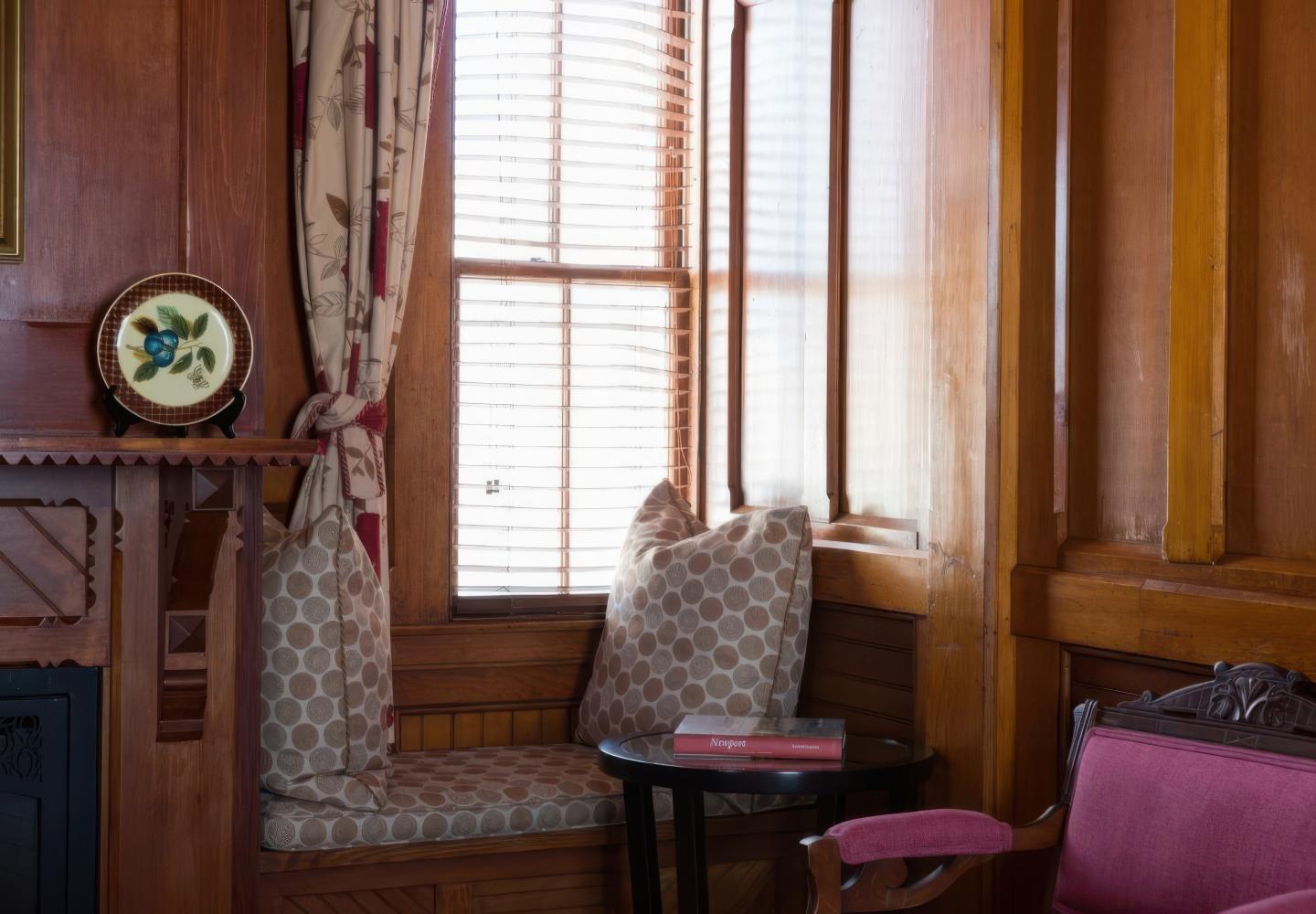 Cozy wooden nook with cushions, small table, and sunlight through blinds.
